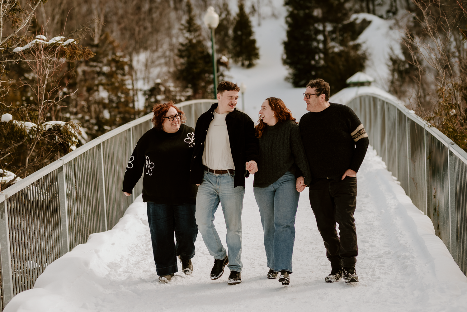 Group of friends walking and laughing together on snowy bridge in winter setting.