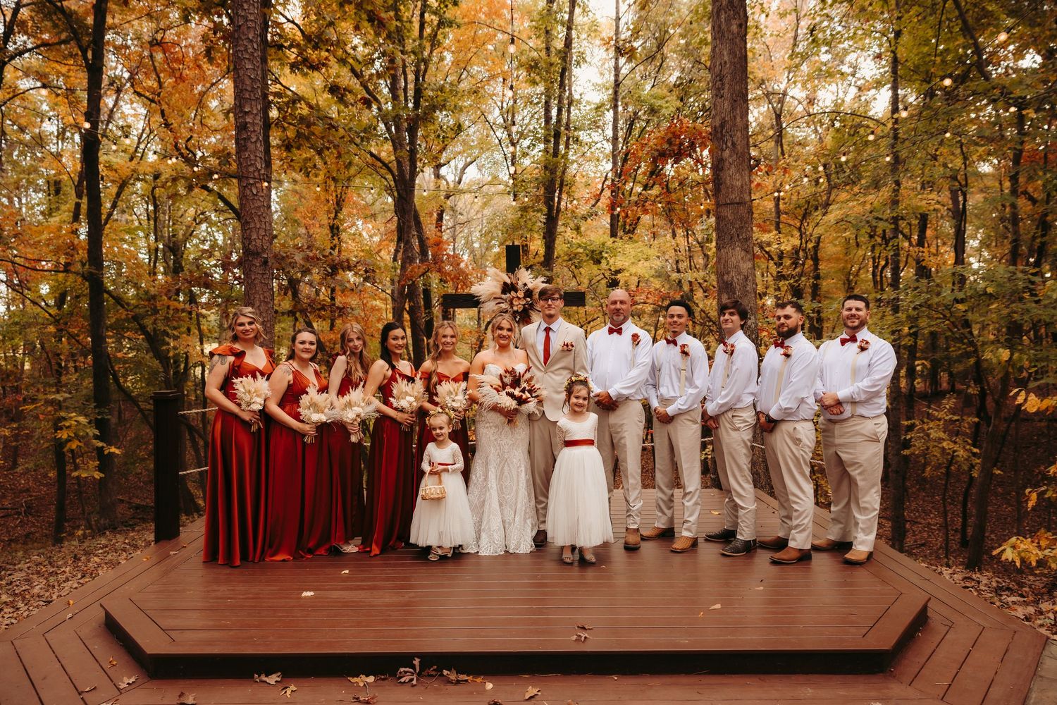Wedding party in burgundy and white attire posed among vibrant fall foliage.