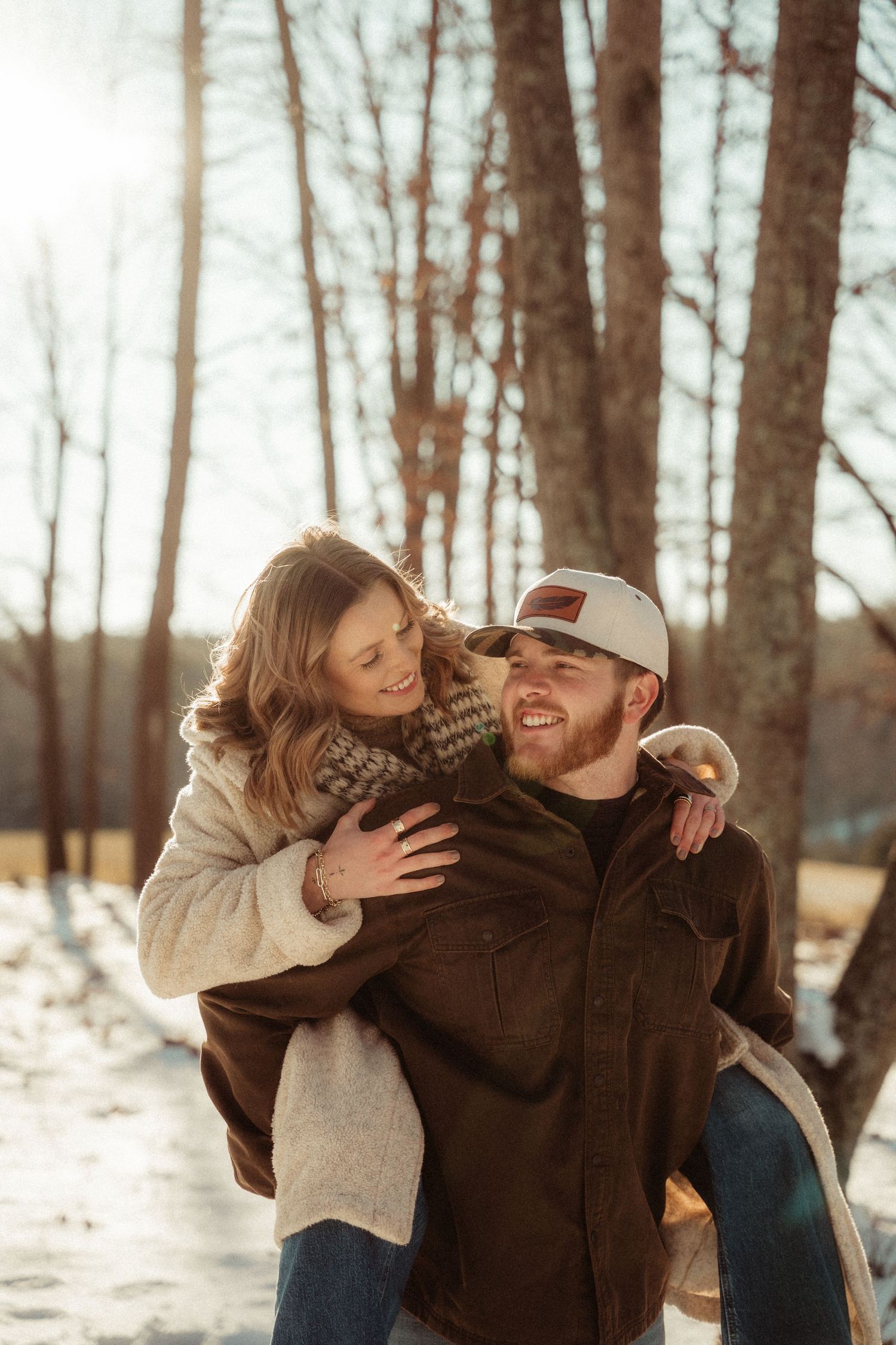 A playful piggyback ride moment between a couple in winter coats among snow-covered trees.
