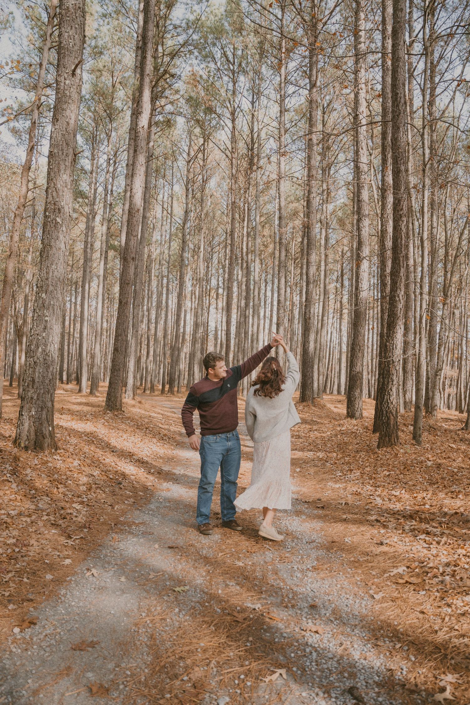 A couple walking hand in hand down a tree-lined path covered in fallen leaves.
