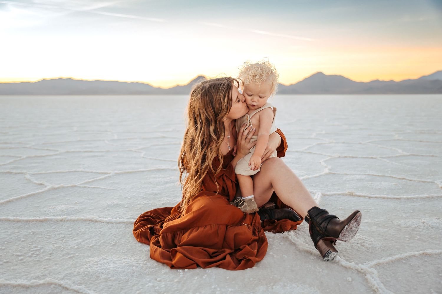 Romantic desert photoshoot with couple in rust-colored clothing against salt flat landscape.