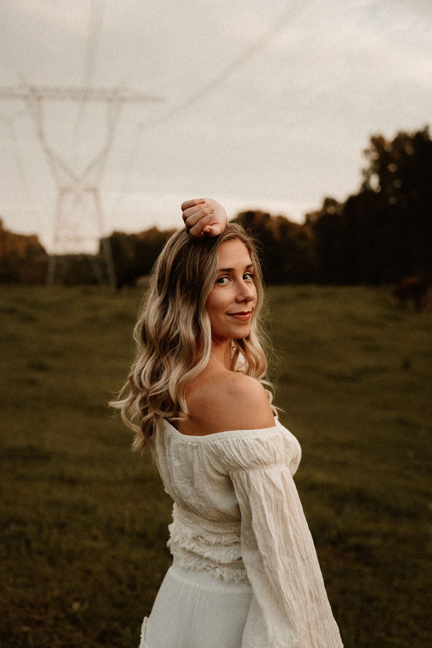 A flowing white off-shoulder dress catches the golden light in a rustic outdoor photoshoot at sunset.
