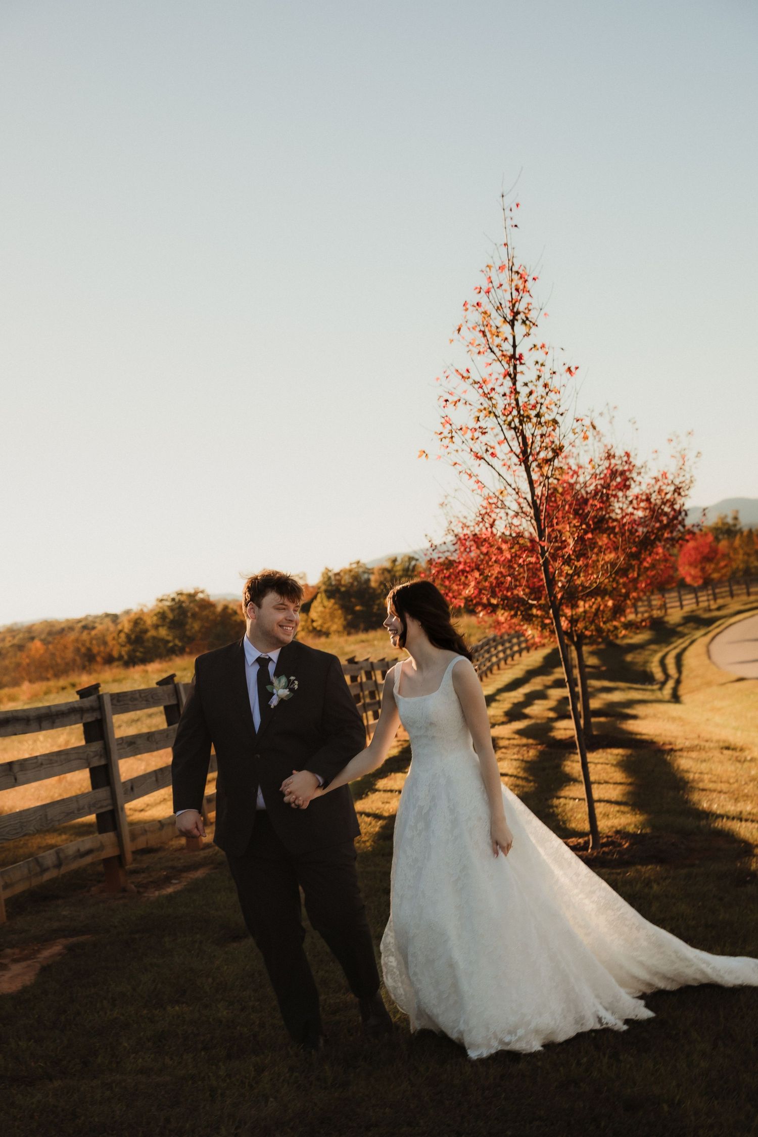 Romantic sunset wedding photos with couple walking along rustic wooden fence.