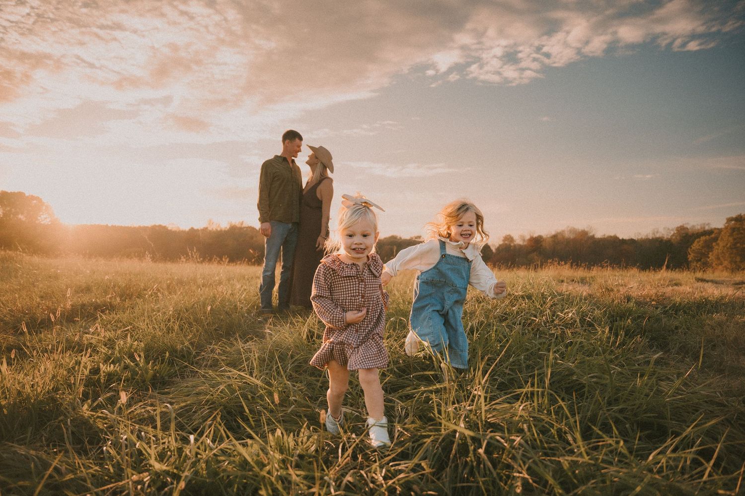 Children playing in field during golden hour with couple in background.