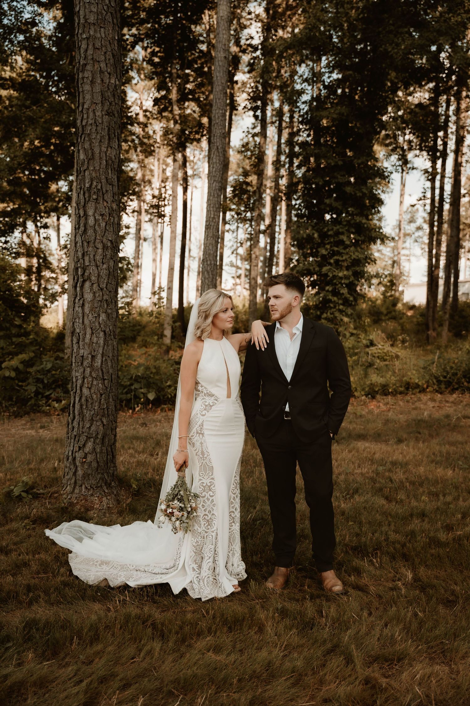 A couple poses together in a serene forest setting during their wedding photoshoot.