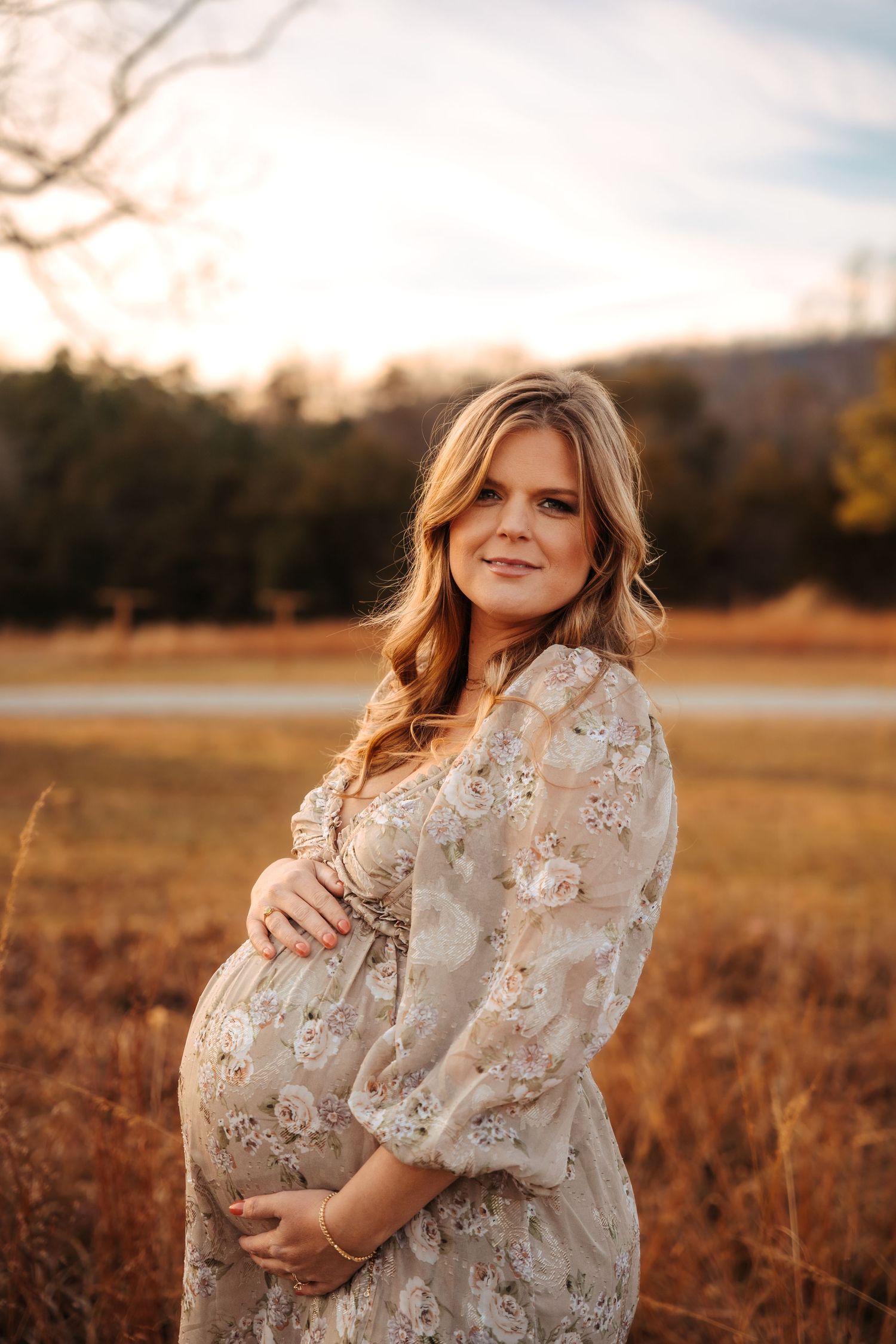 Maternity photos in a golden field at sunset with woman wearing floral dress.