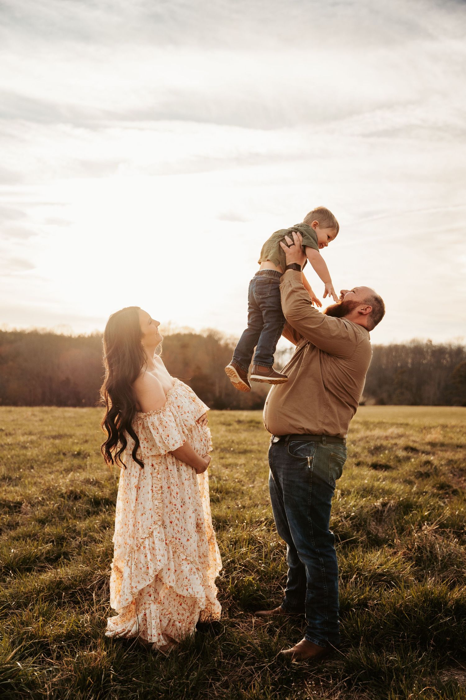 Family enjoying sunset in field as parents play with child against golden sky.