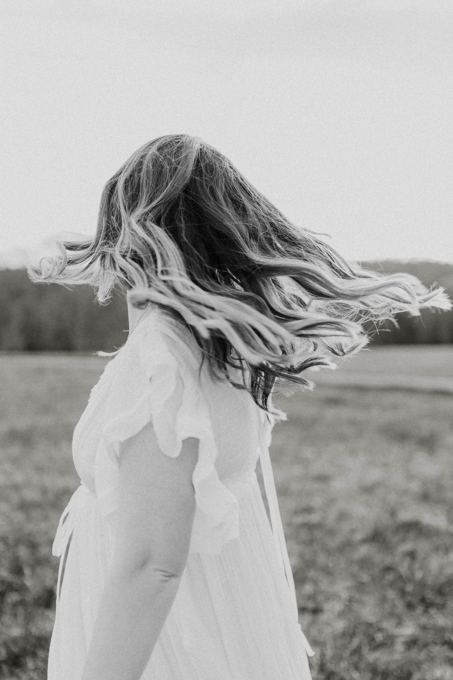 Black and white photo of flowing hair and dress movement captured in a field.