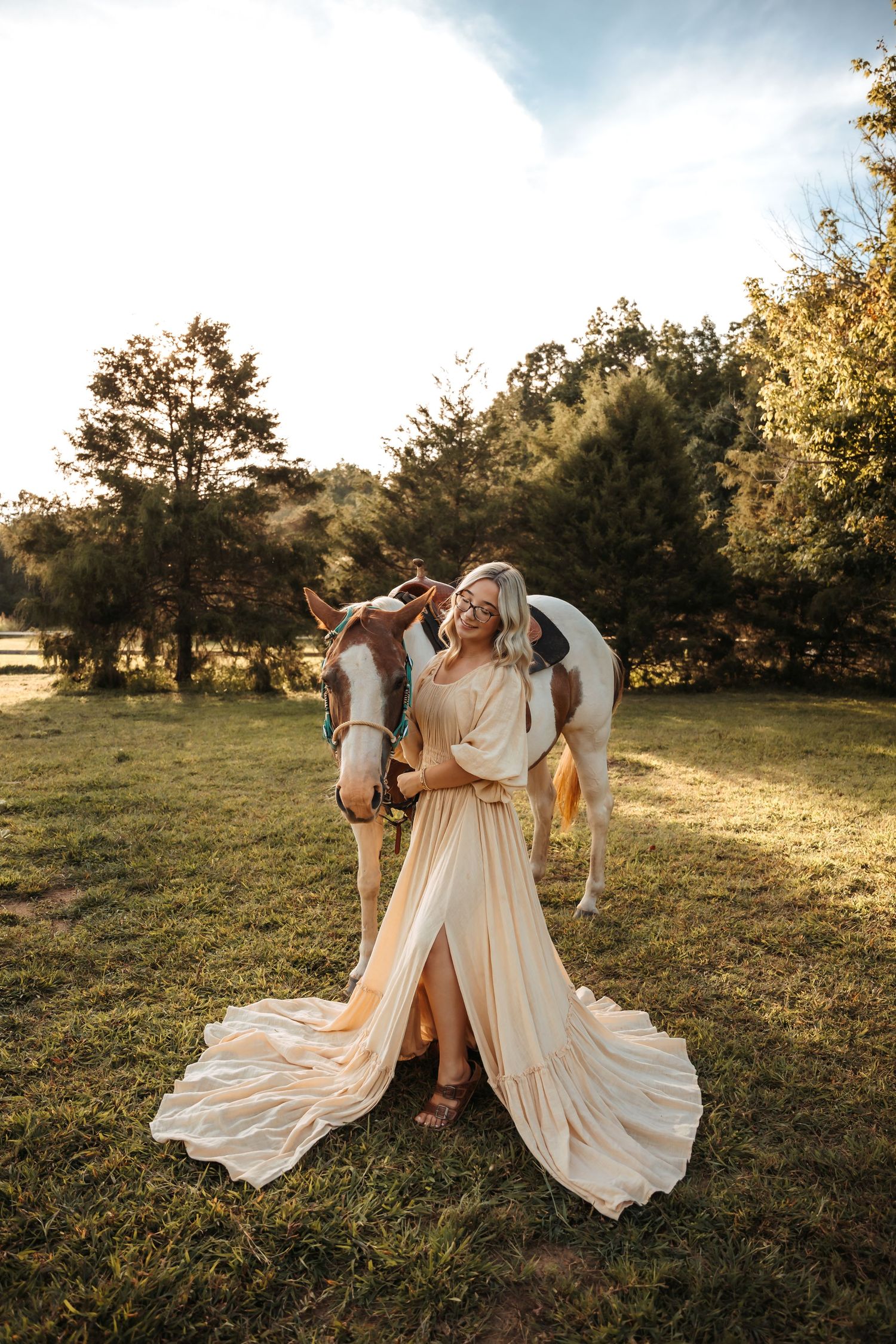 A flowing white dress catches the sunlight in a golden field with a horse at sunset.