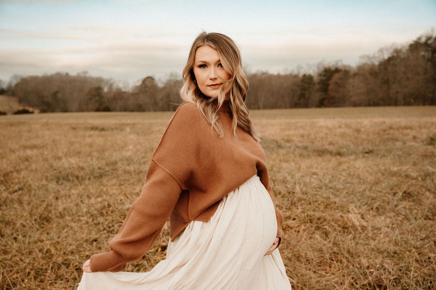 Woman in white dress poses in golden field during sunset.