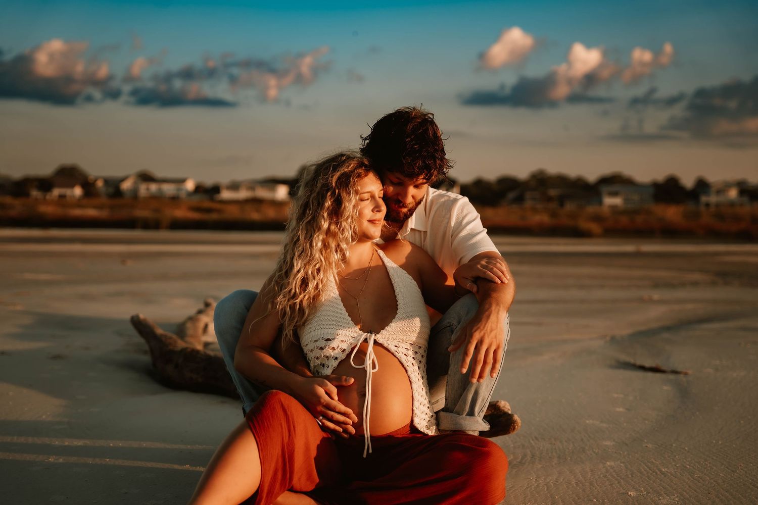 Couple shares intimate moment on beach at sunset with dramatic sky.