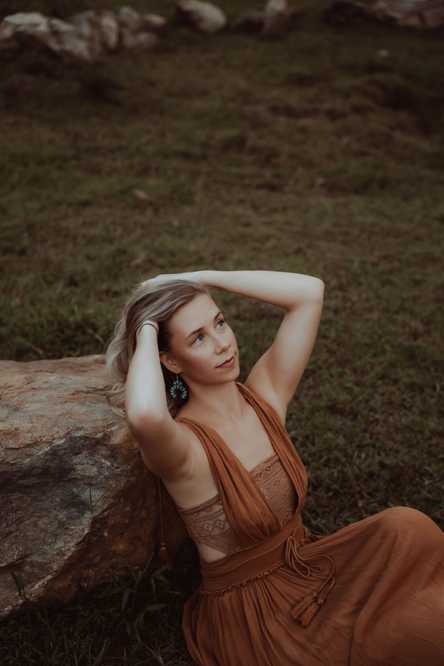 A brown vintage-style dress creates dramatic contrast against natural stone in moody outdoor portrait.