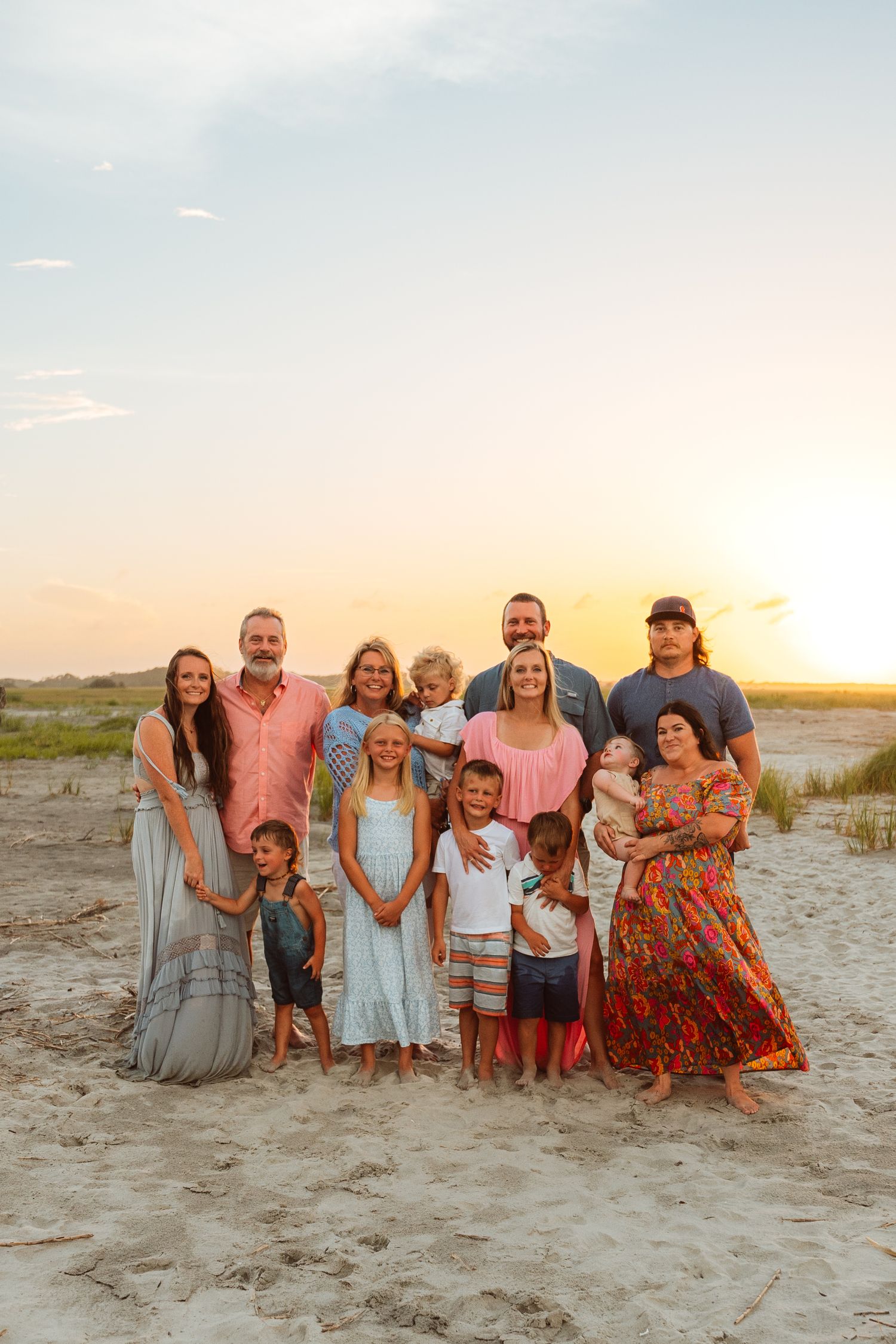 Extended family group portrait on sandy beach at sunset wearing coordinated casual outfits.