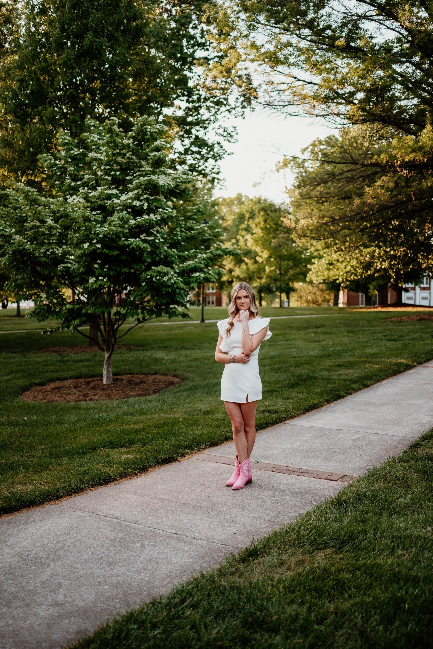 White summer outfit and pink shoes create contrast along a tree-lined concrete pathway.