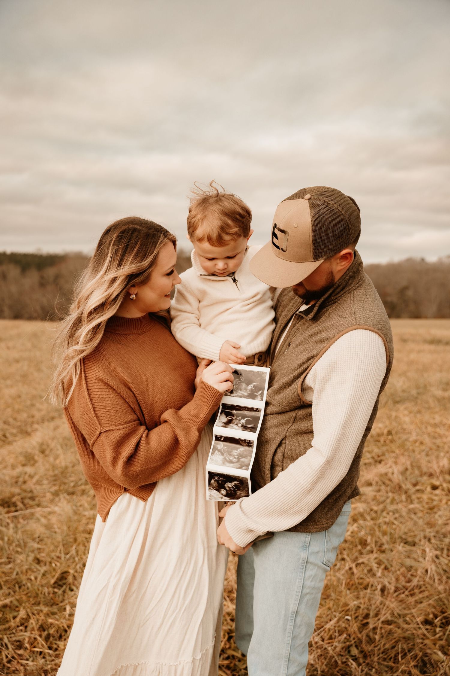 Family shares special moment while looking at ultrasound photos in autumn field.