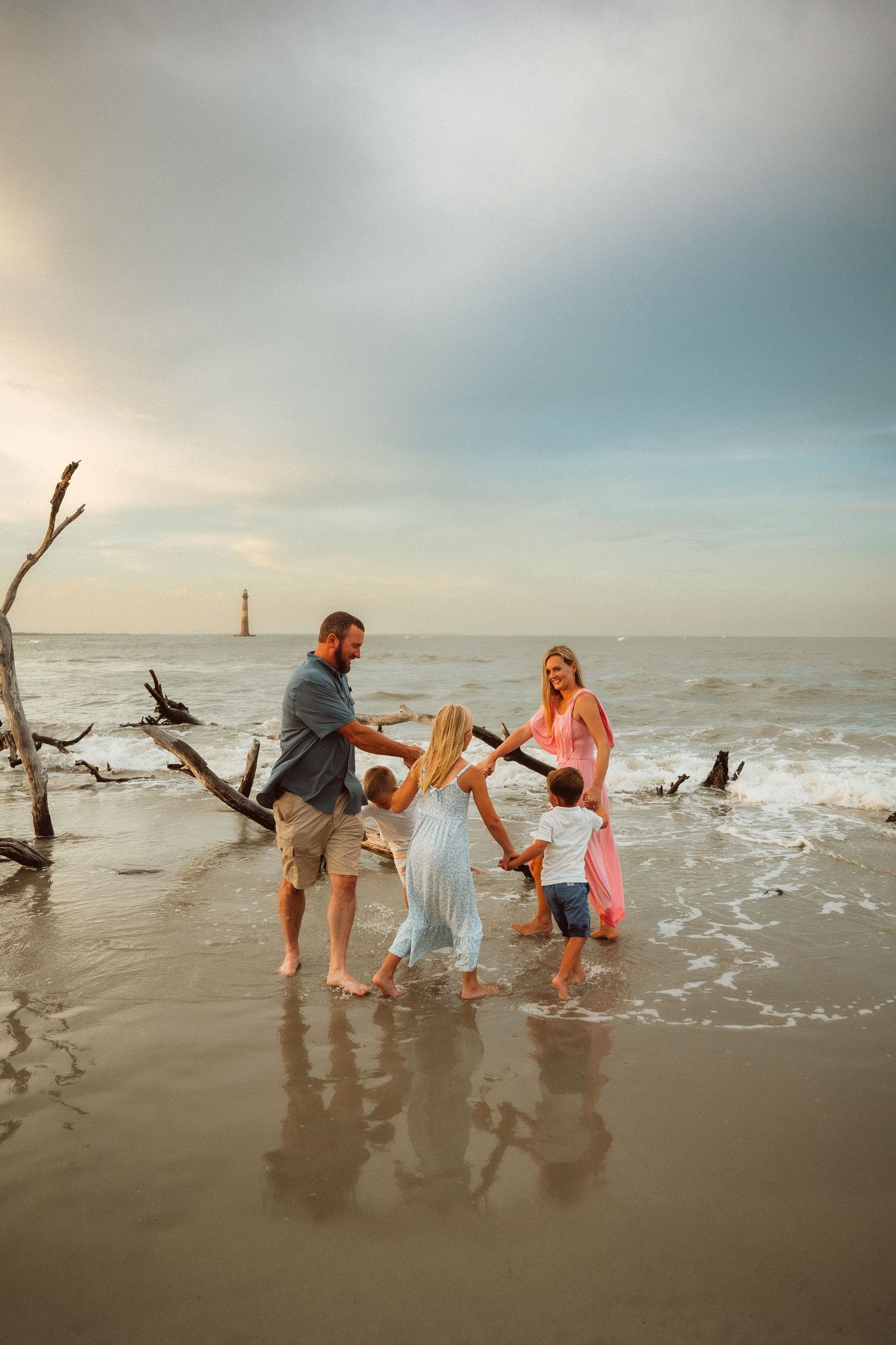 Family playing and splashing together in ocean waves at sunset near driftwood on beach.