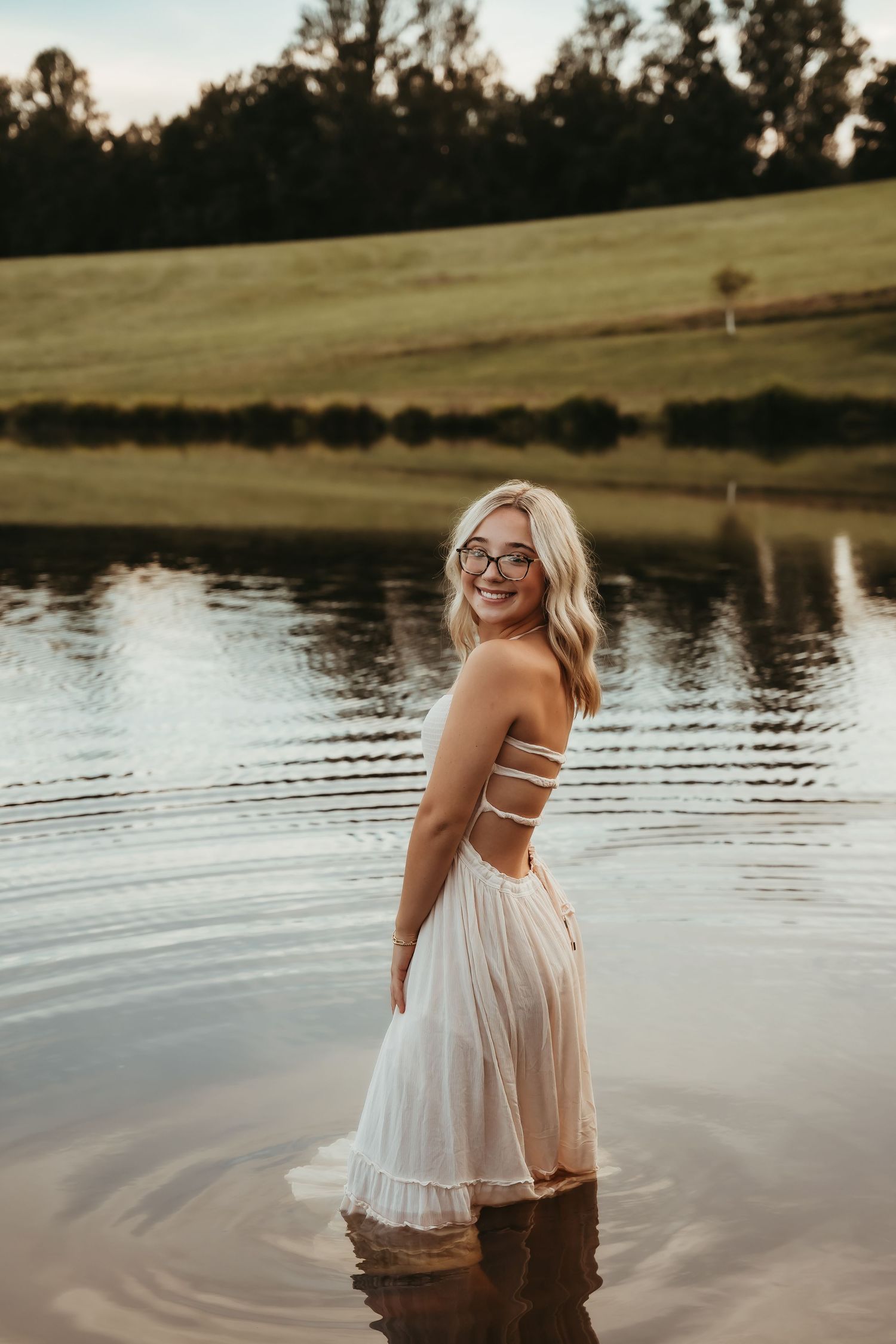 A white sundress reflects in calm lake waters during a summer photoshoot.
