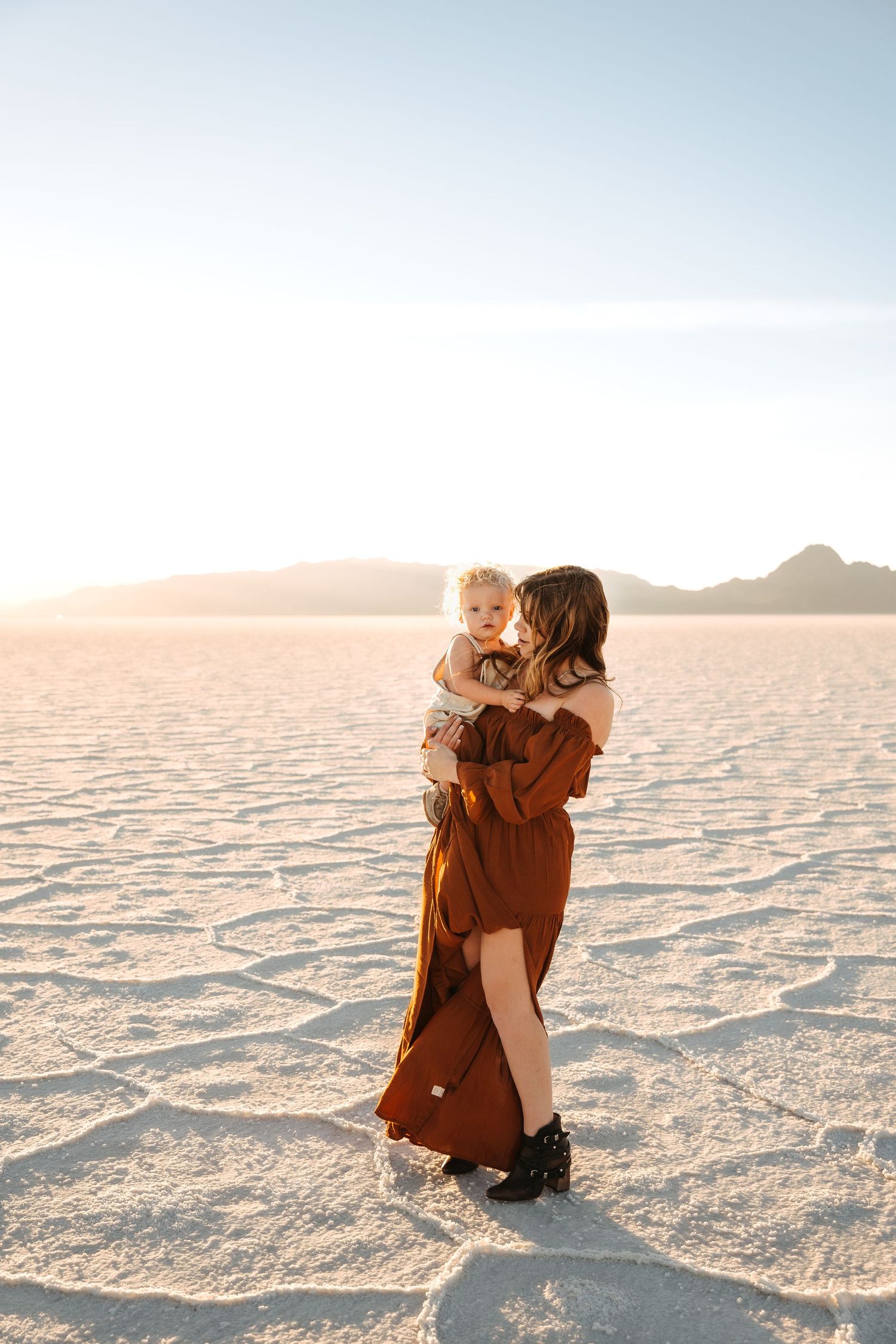 Couple in flowing outfits poses dramatically on white salt flats during golden hour.