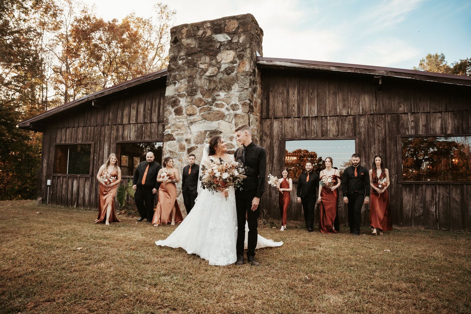 Wedding party photo at rustic barn venue with stone chimney in autumn.