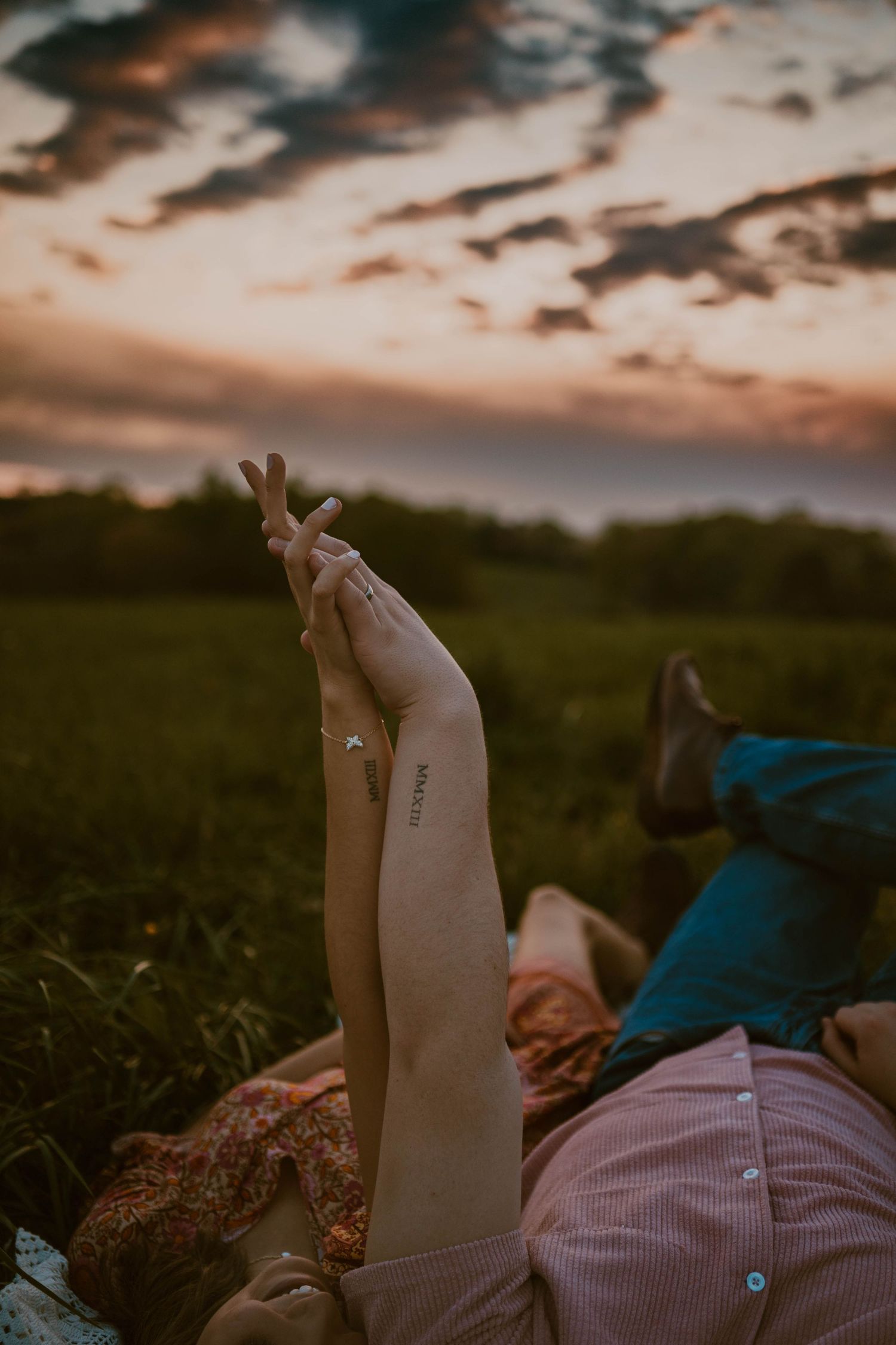 Someone relaxes in a field during sunset with dramatic clouds overhead.