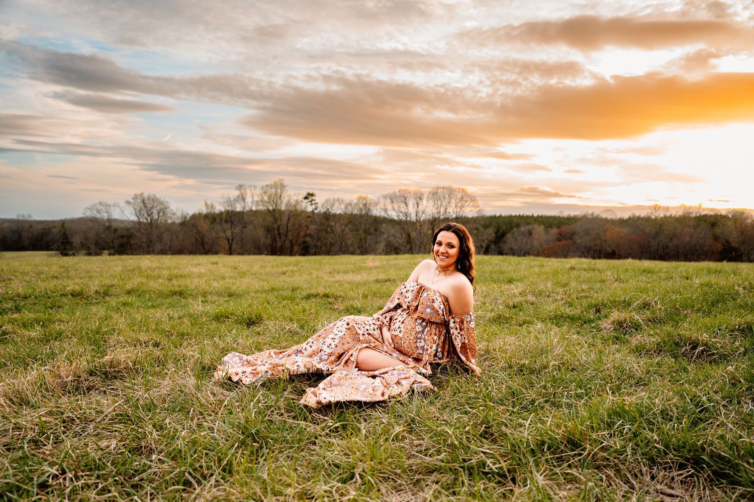 Scenic sunset maternity session in an open field with golden light.