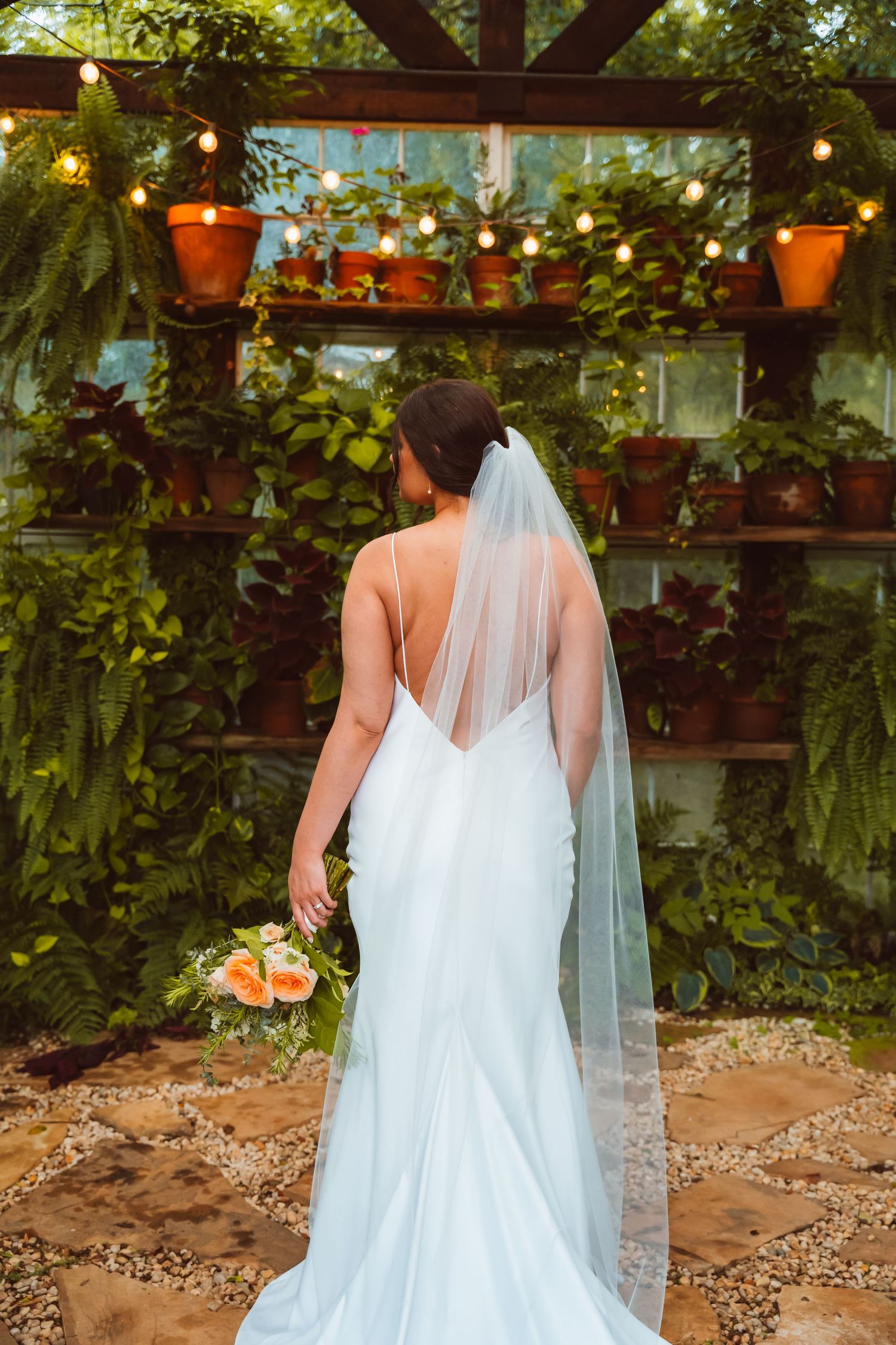 White wedding dress with sheer veil detail in a garden setting with hanging plants.