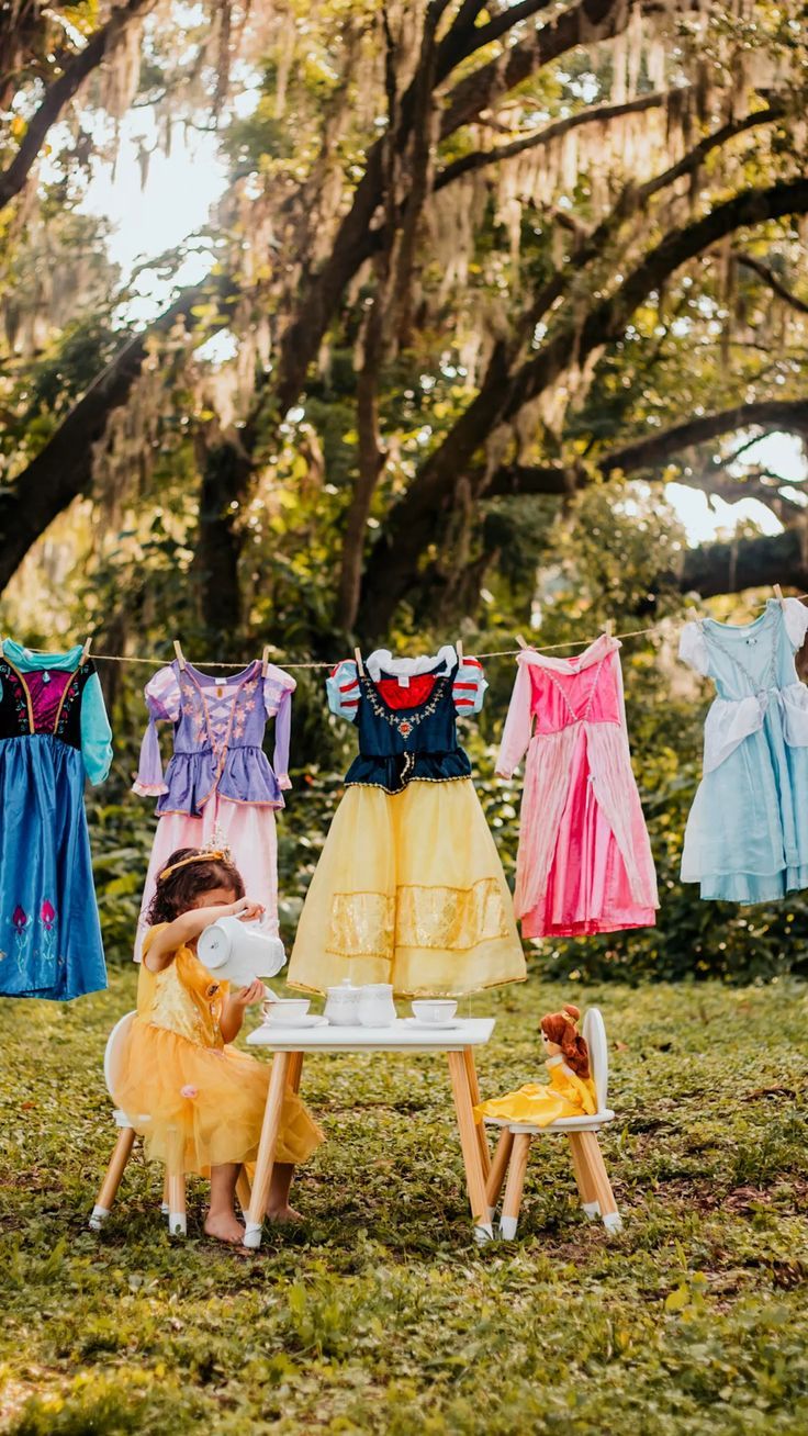 Colorful princess dresses hanging on a clothesline between trees with Spanish moss in a sunny garden.
