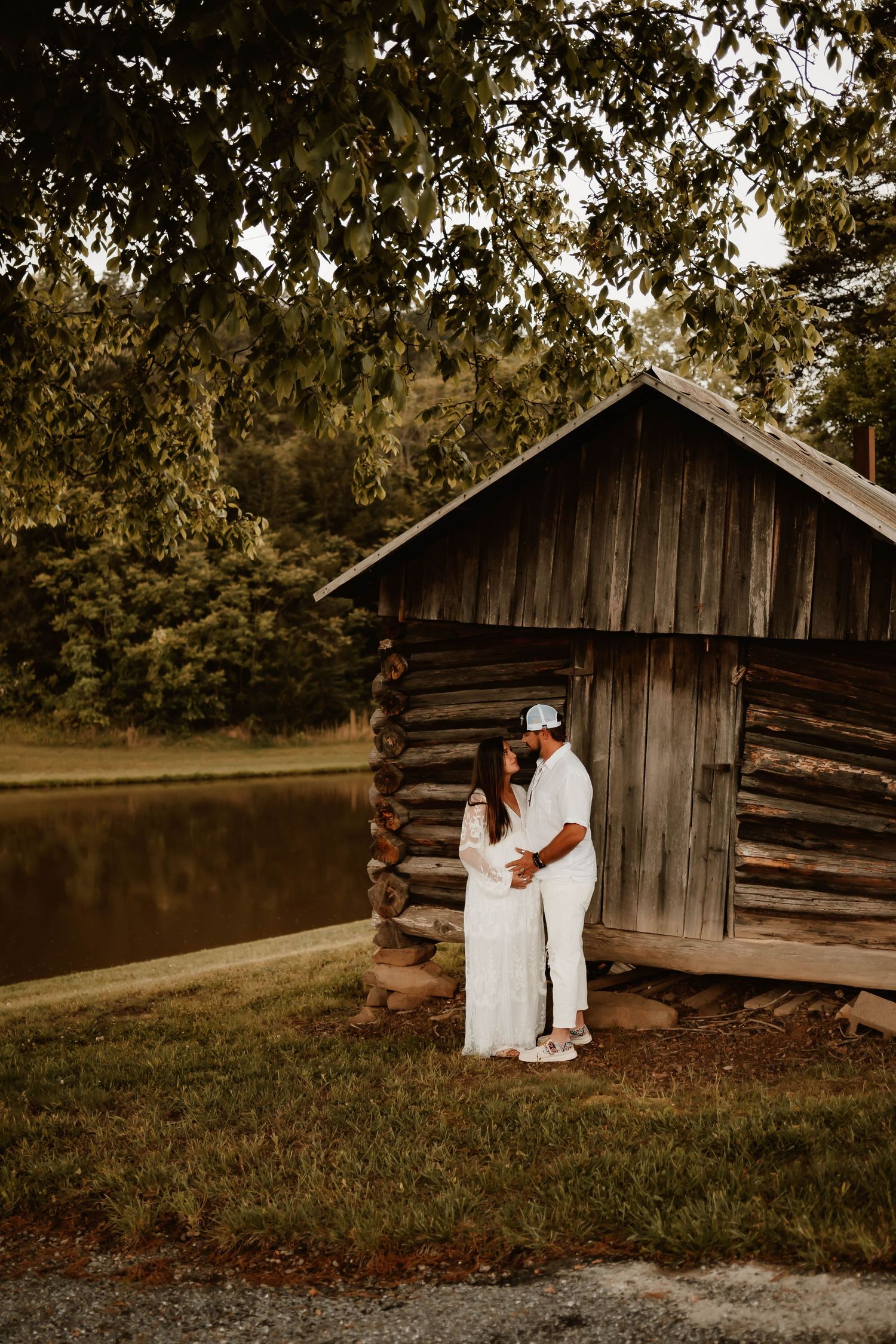 A rustic maternity photoshoot near a weathered wooden barn in sepia tones.