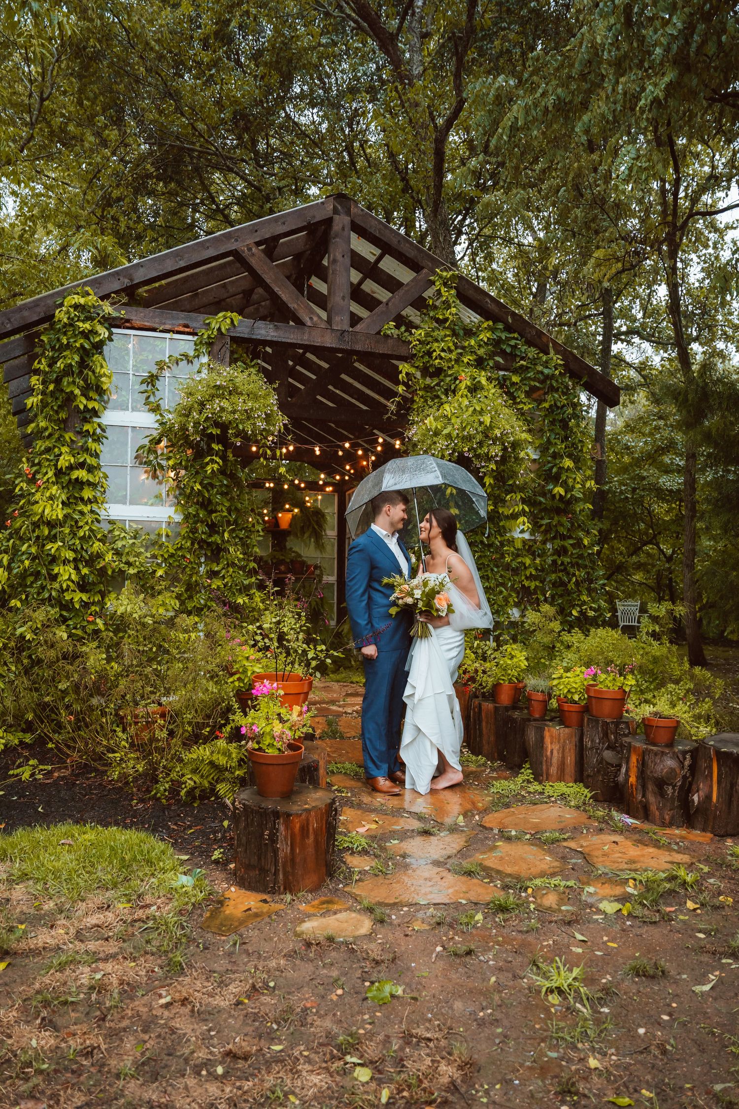 Garden wedding venue with stone pathway and wooden gazebo surrounded by greenery.