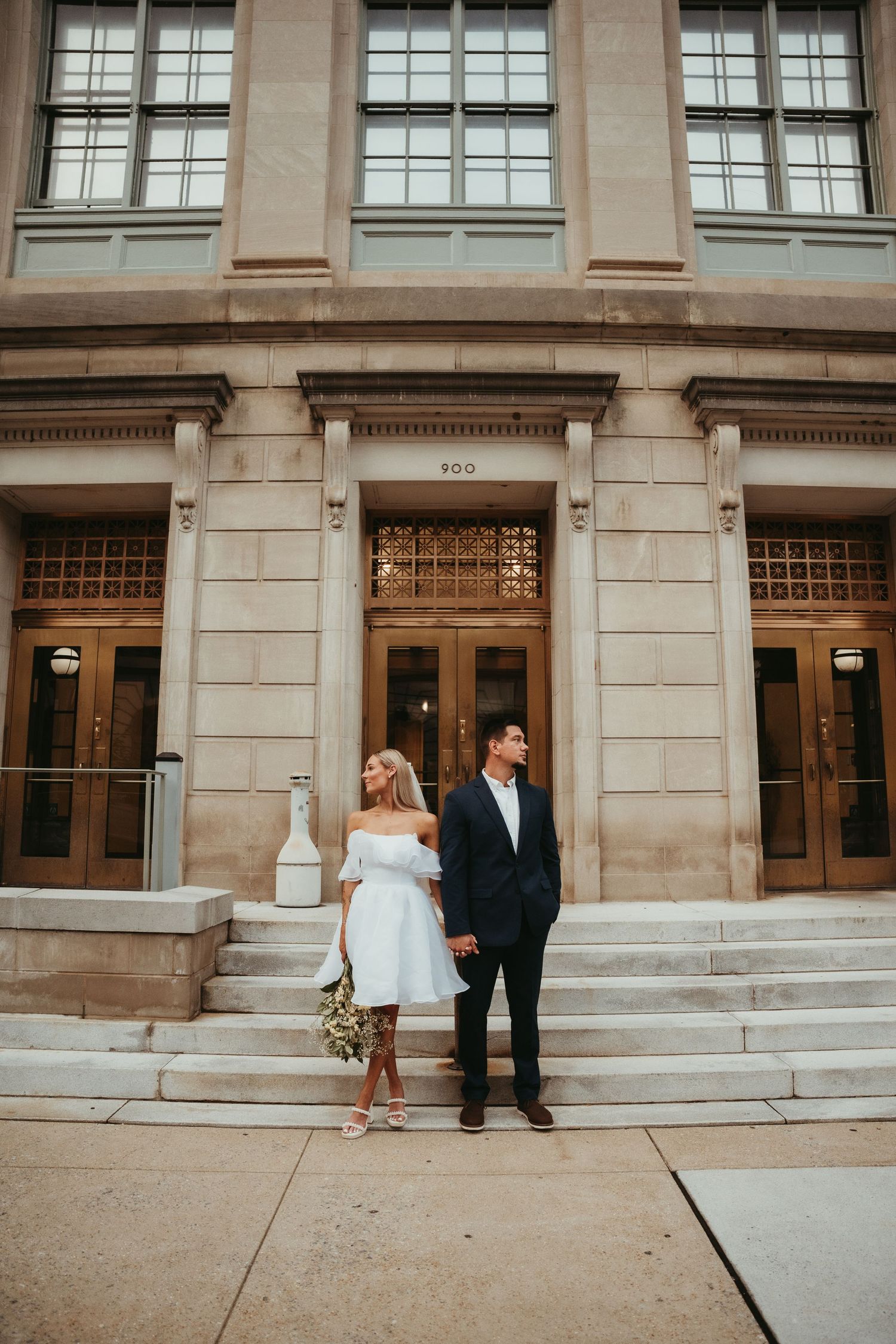 Wedding portraits in front of classic stone building with large windows and ornate details.