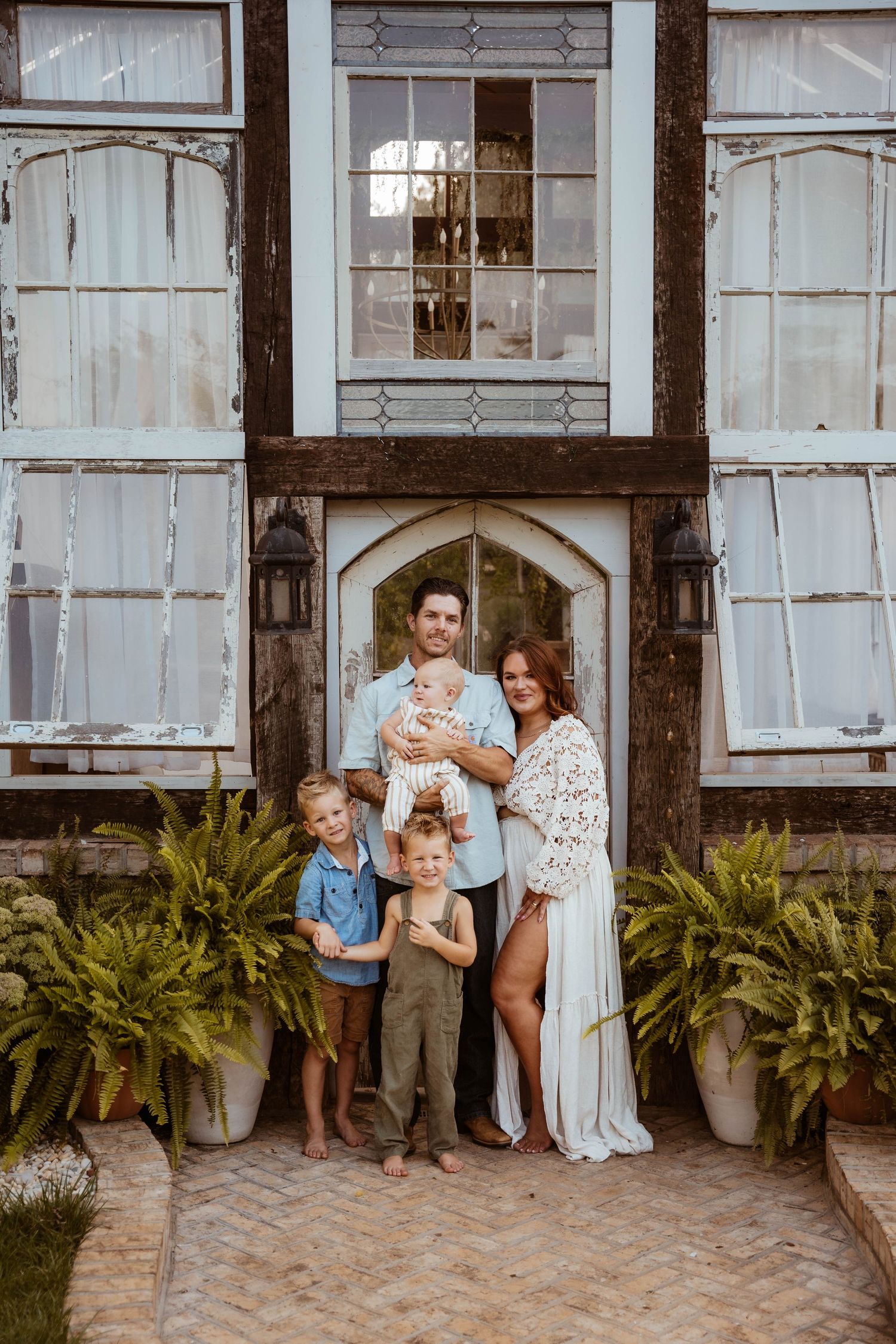 Charming white farmhouse exterior with vintage windows and potted ferns along the porch.