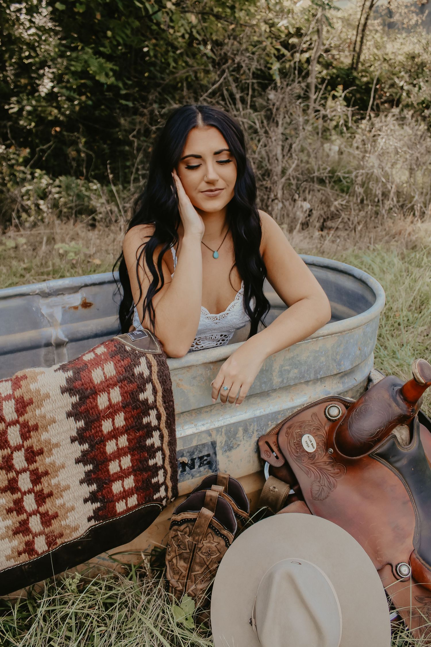 Relaxed portrait in stock tank with western accessories and blanket nearby.