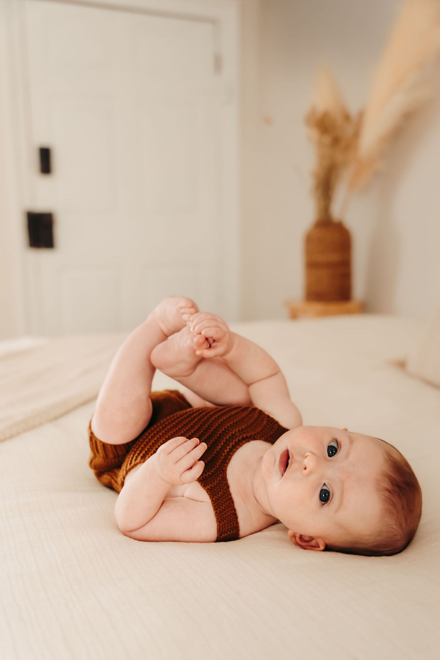 Baby in brown outfit lying on white surface in minimalist indoor setting.