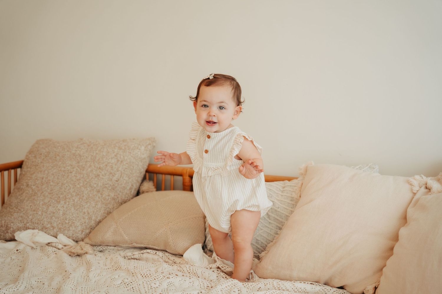 Baby milestone photography session on a beige couch with neutral decor.