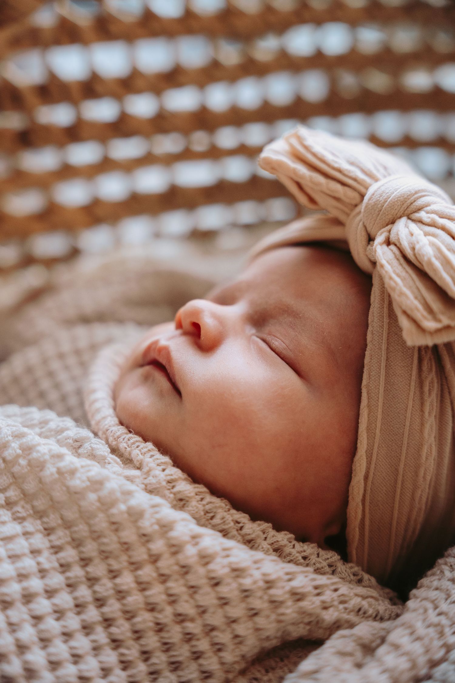 Close-up of sleeping newborn wearing soft beige headband on textured blanket.