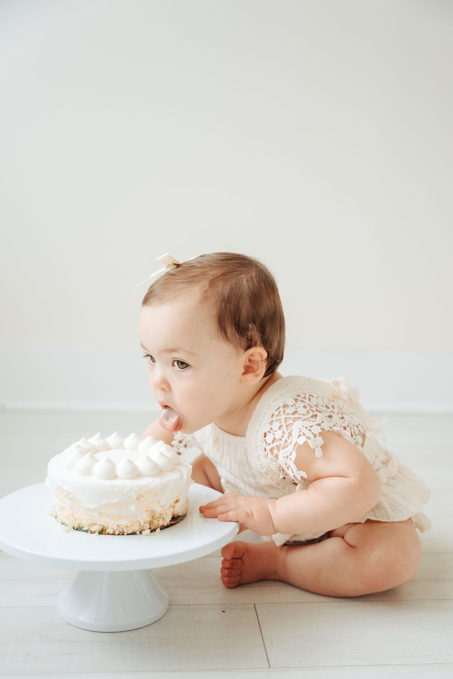 Minimalist white cake smash photo setup on wooden floor.