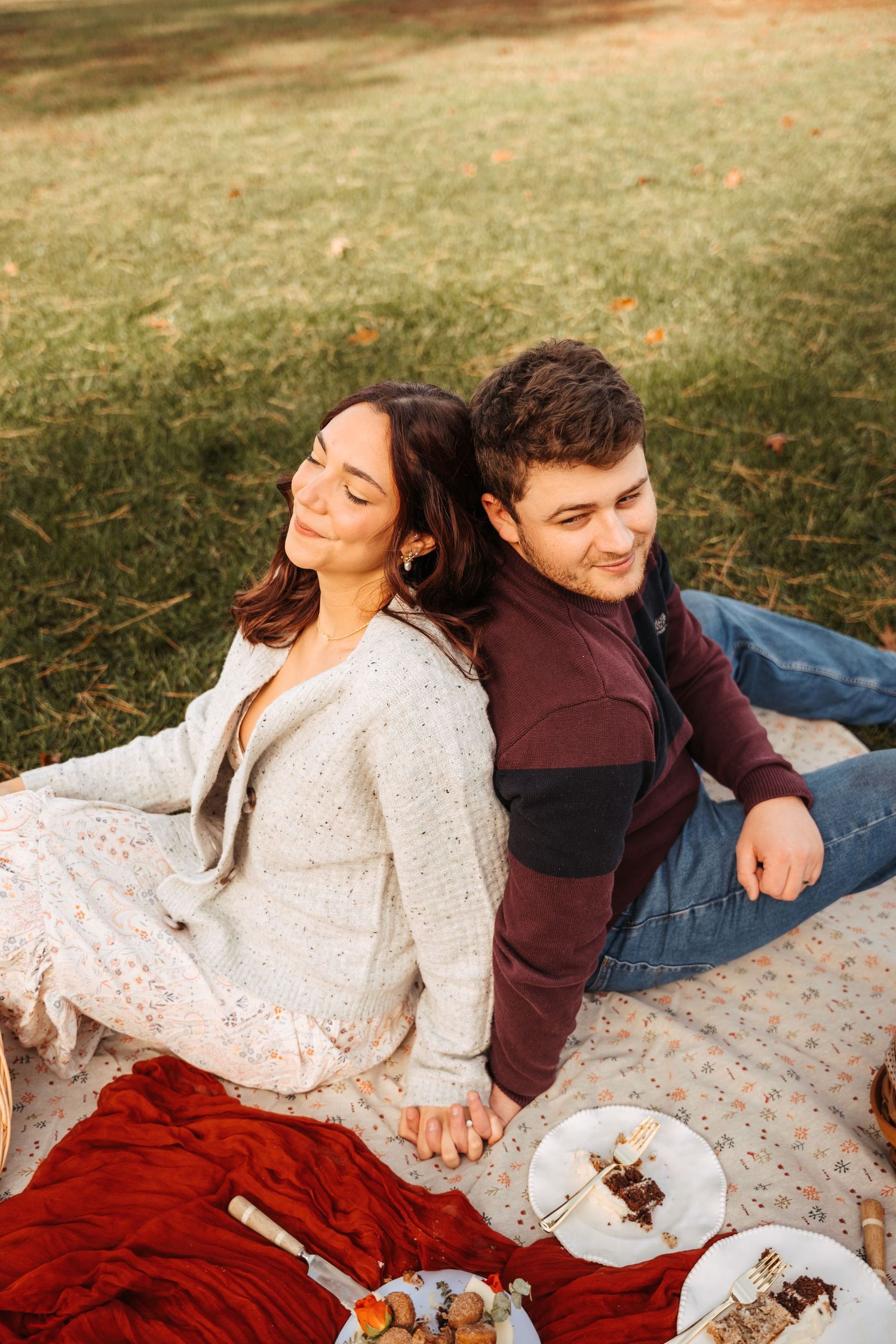 A couple enjoying a romantic picnic with red blanket and snacks.