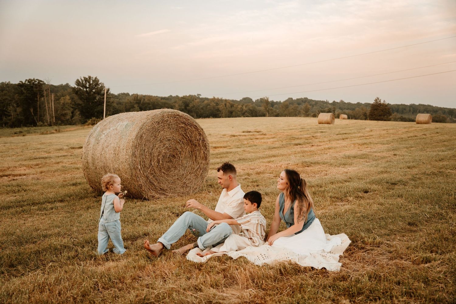 Family enjoying a golden sunset in a field with hay bales during a rustic outdoor photo session.