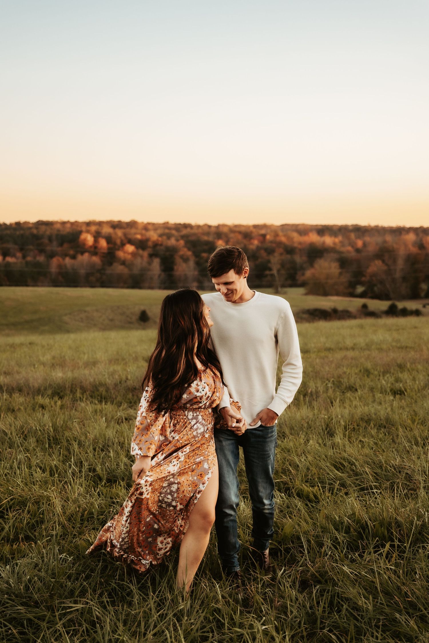 A couple standing together in a field during golden hour.