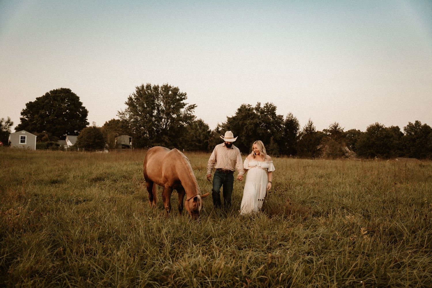 Horse grazes in field while couple walks together at dusk.