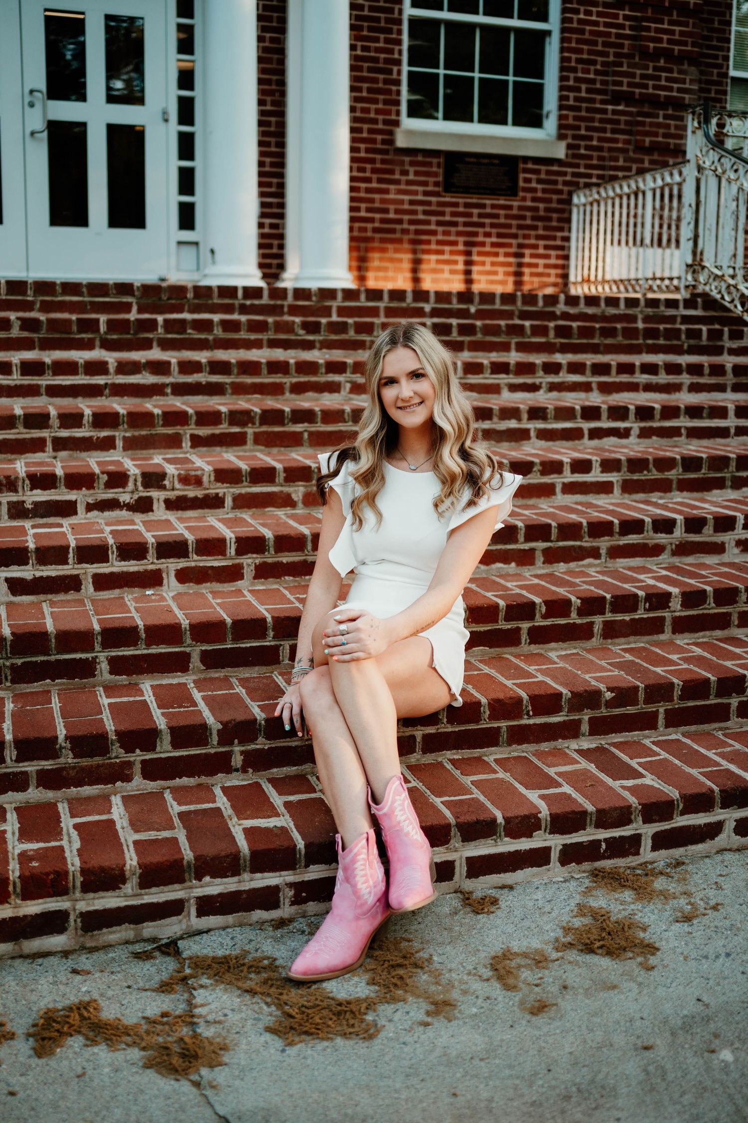 Pink boots add a pop of color against brick steps in a casual outdoor portrait session.