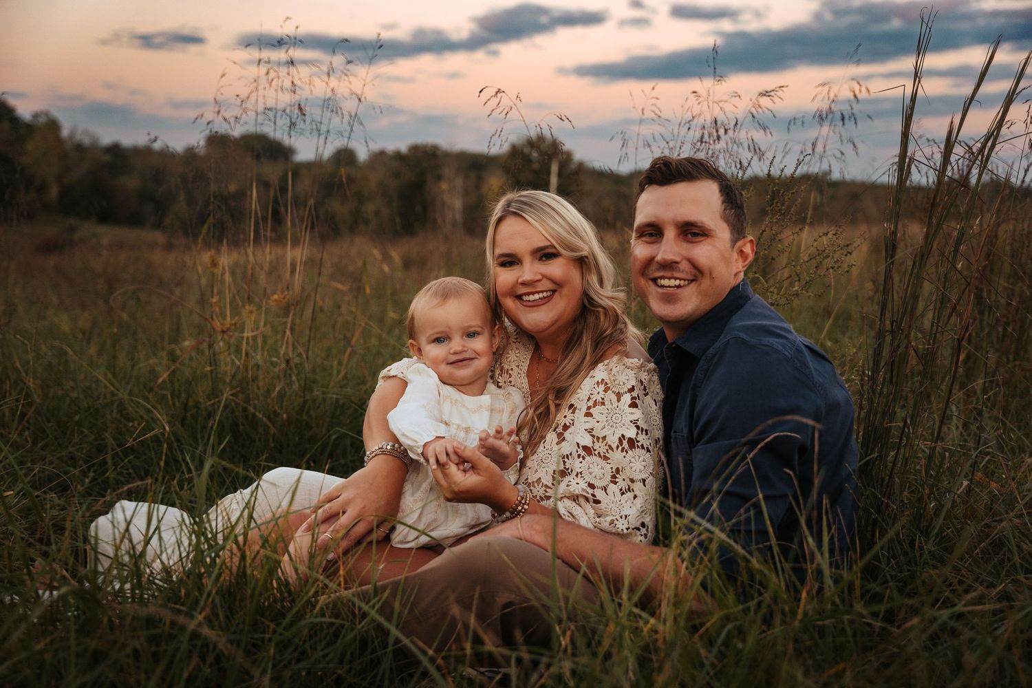 Family cuddling together in a field at sunset with warm lighting.
