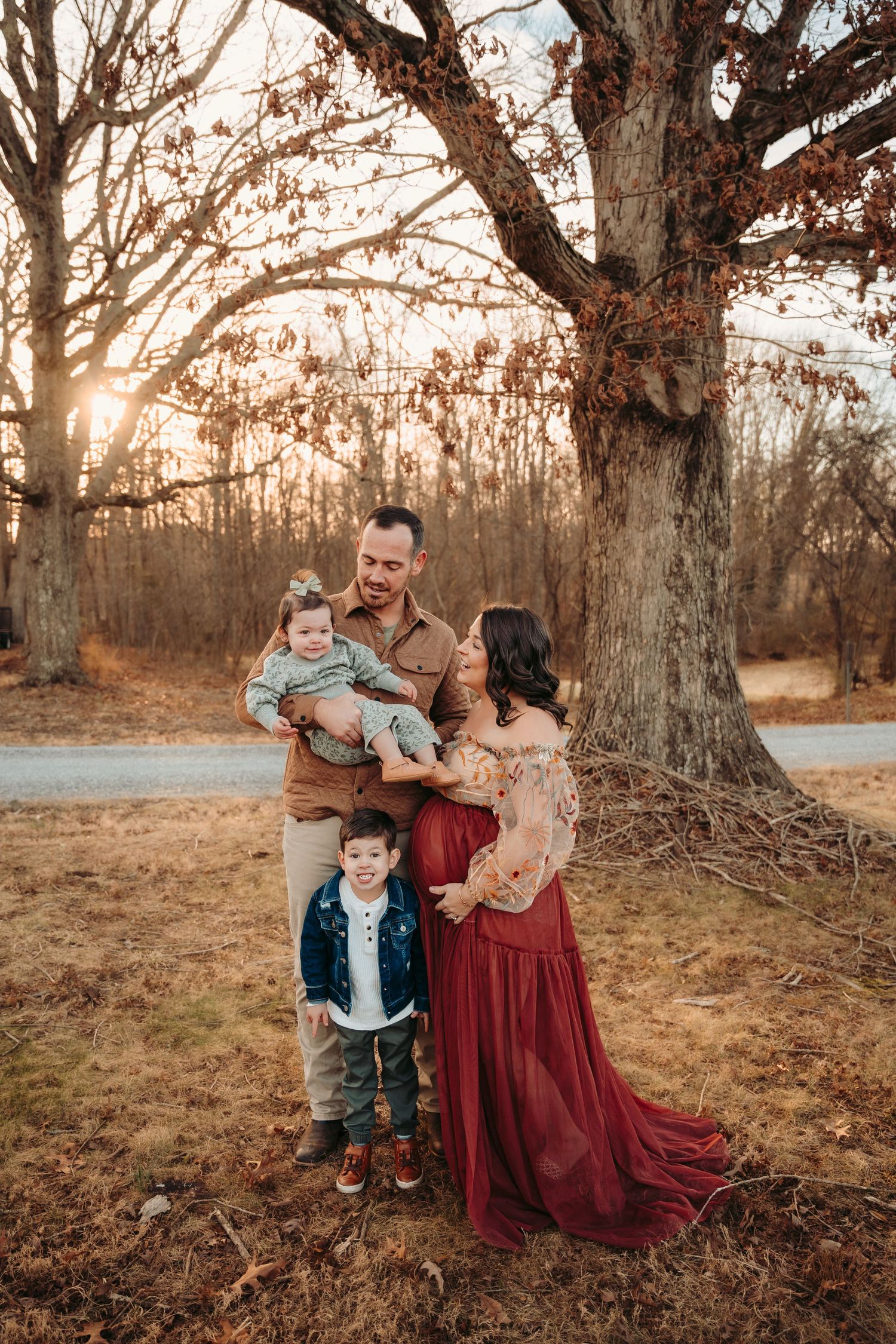 Family poses together under autumn trees at sunset wearing burgundy and brown coordinating outfits.