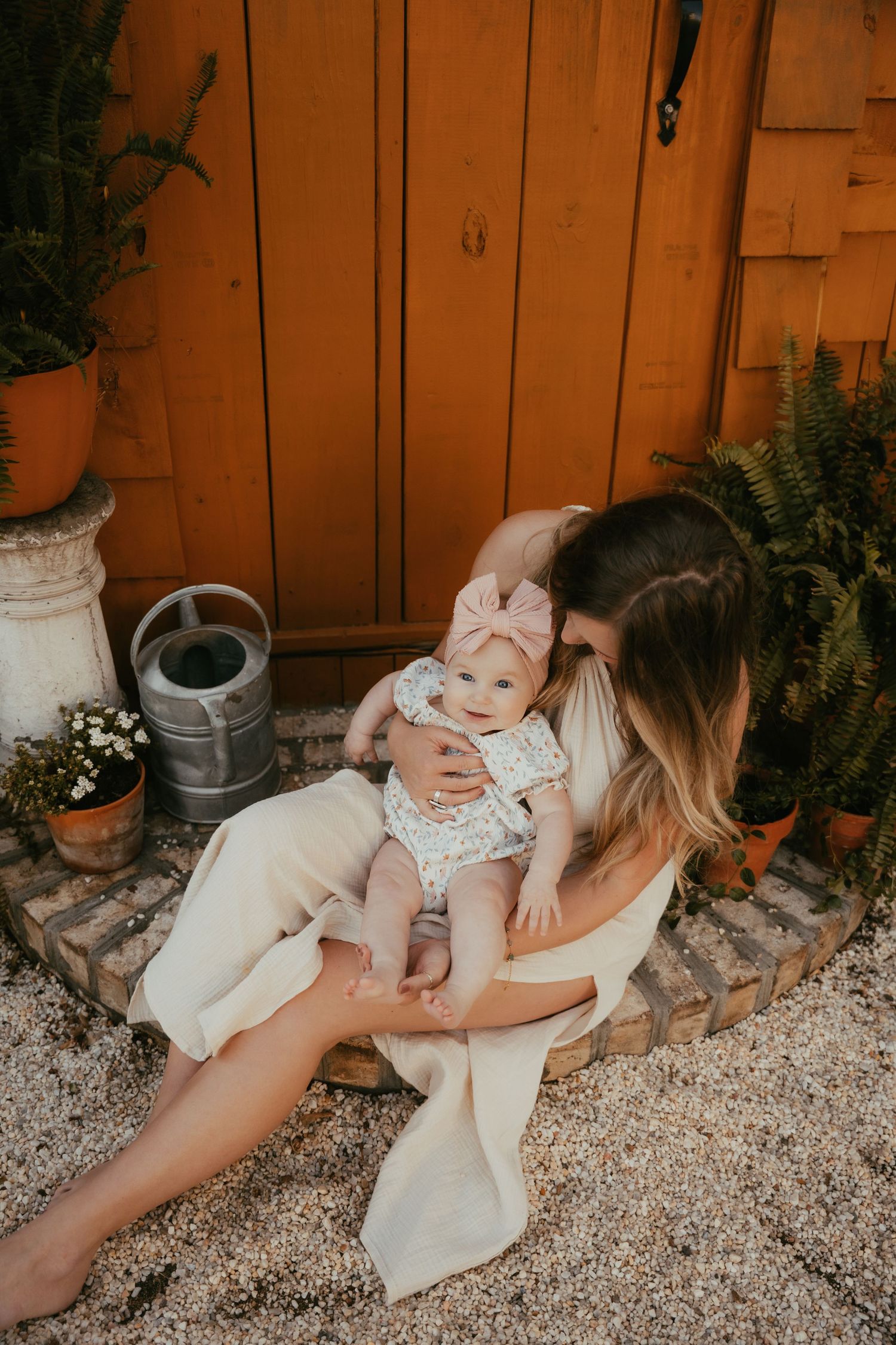 Parent and child share tender moment against orange wooden wall with plants.
