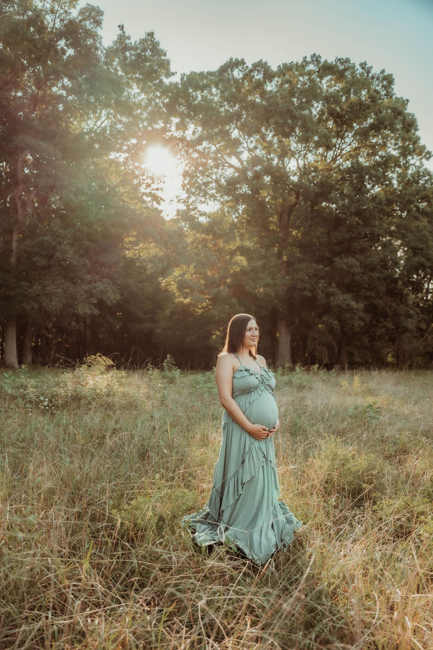 Woman in teal dress poses in sunlit meadow during golden hour.