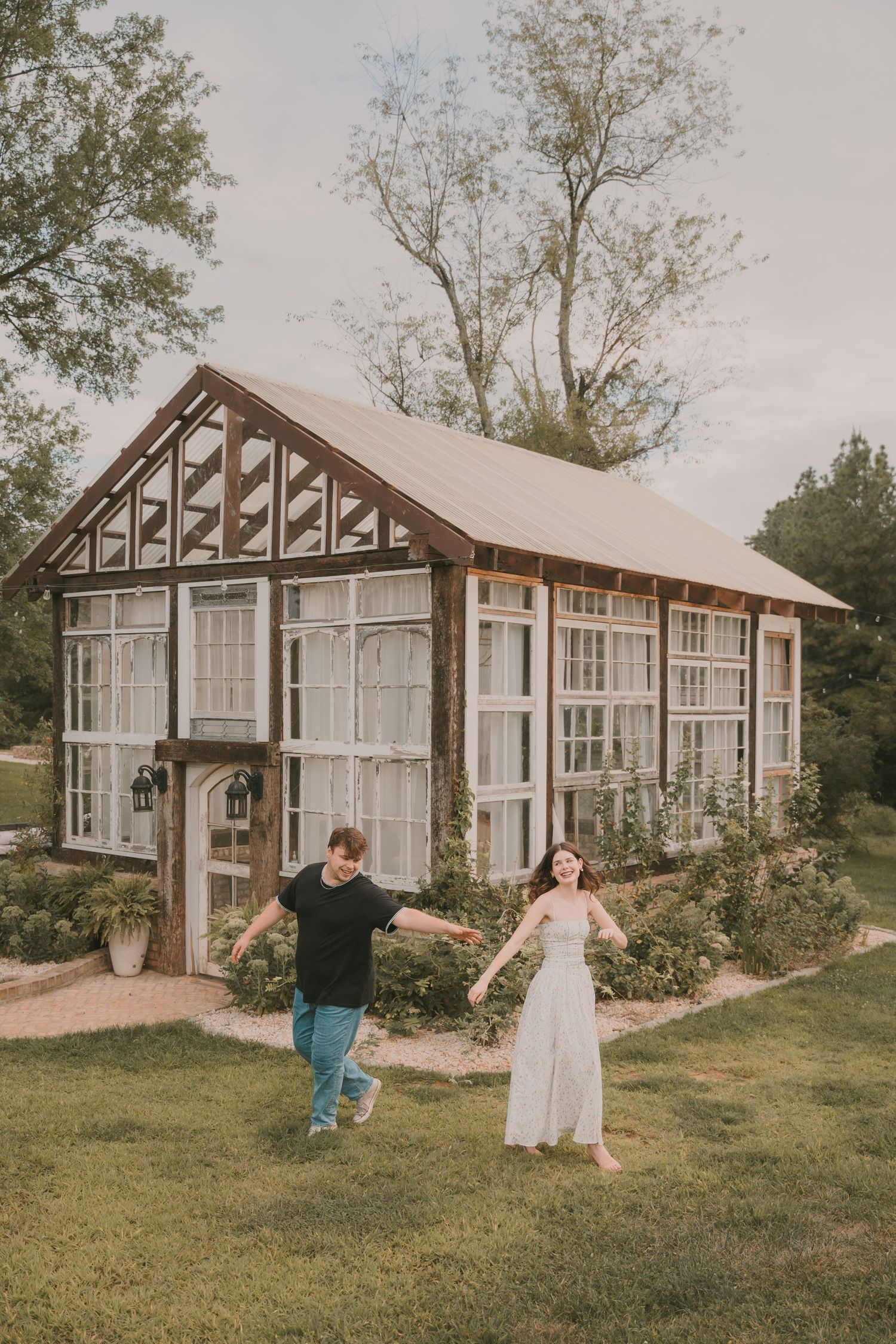 A charming greenhouse structure with white frame sits on a grassy hillside.