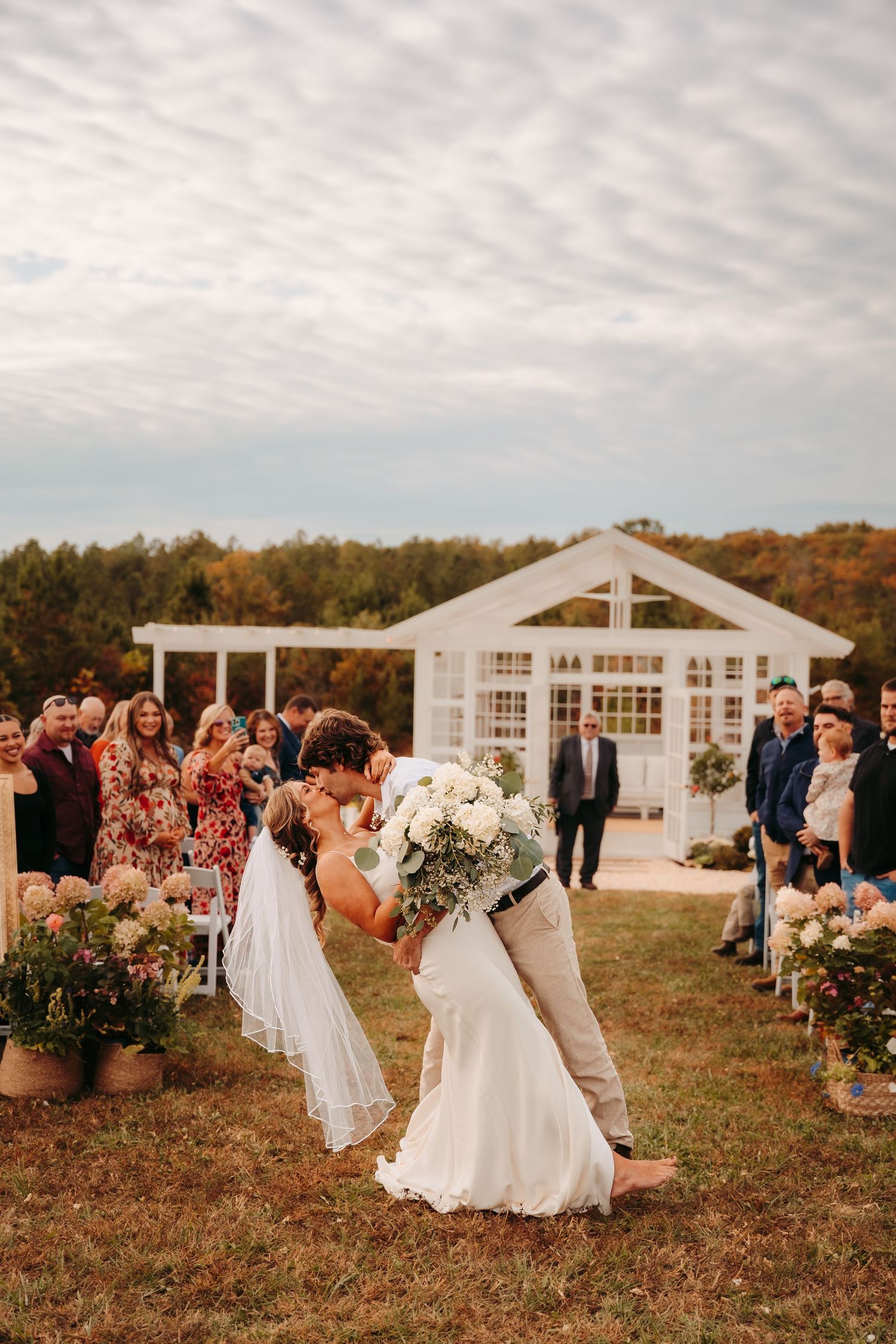 Outdoor wedding ceremony at white pavilion venue with guests seated on both sides.