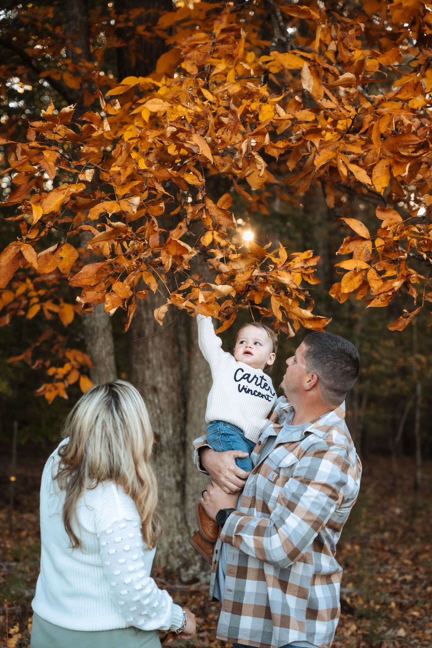 Family playing under golden autumn leaves during outdoor photo session.