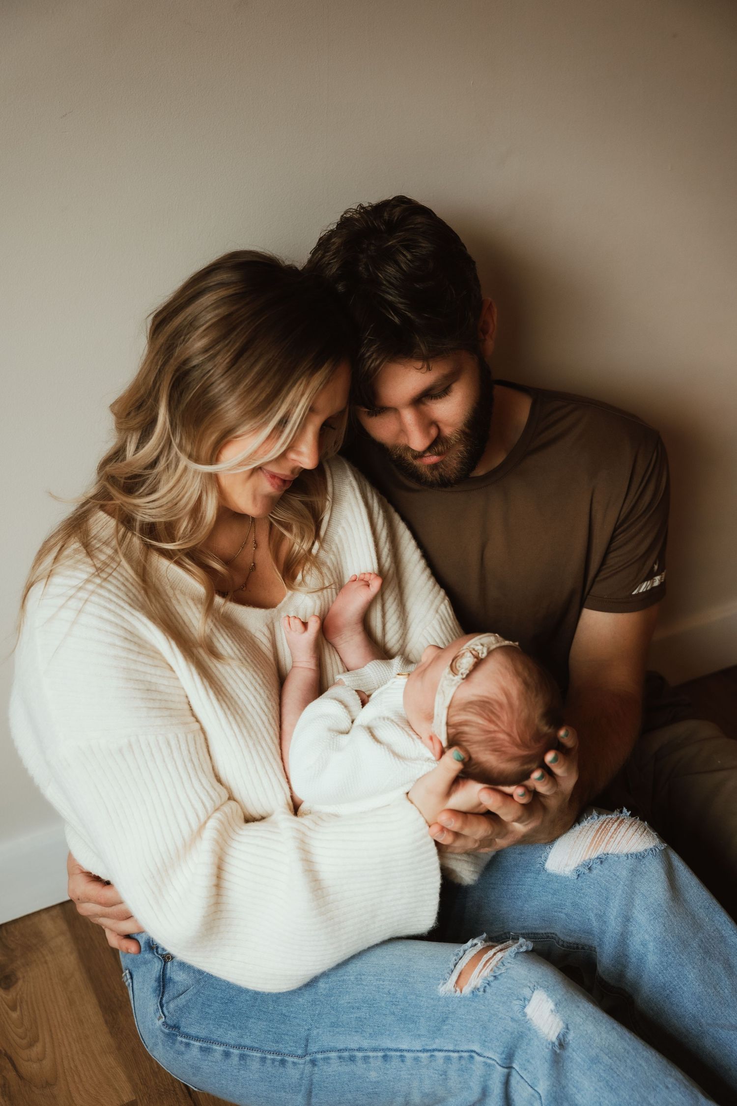 Parents sharing intimate moment with newborn baby on wooden floor.