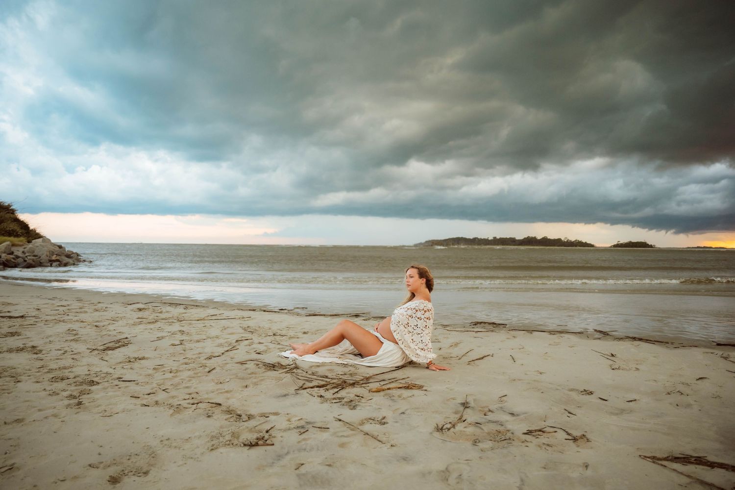 Dramatic coastal photoshoot with stormy skies and sandy beach landscape.